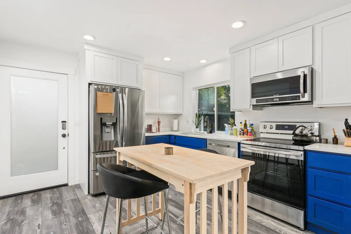A bright and inviting kitchen area with a central island, striking blue cabinets, and stainless steel appliances. Natural light fills the space, suggesting a modern yet welcoming environment perfect for cooking, socializing, or simply enjoying a cup of coffee.
