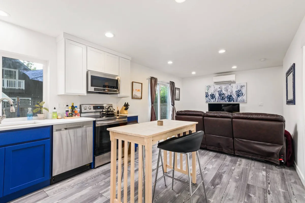 The image showcases a bright, open-concept living space featuring a stylish kitchen island with a sink, a cozy couch perfectly positioned for relaxation, and tasteful artwork adorning the walls. The inviting setup highlights ample space for cooking, dining, socializing, and unwinding—all bathed in welcoming natural light.