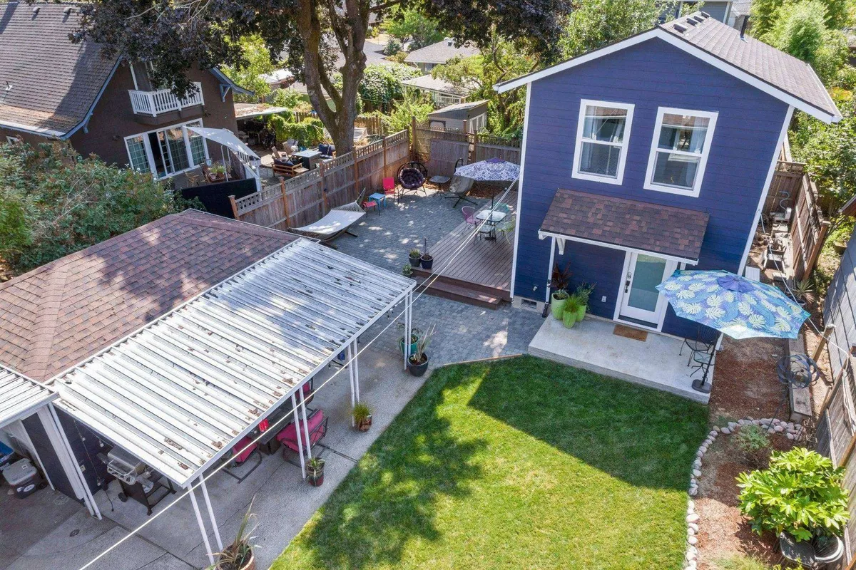 A vibrant exterior shot featuring a purple house, a spacious deck area with varied seating arrangements, and a landscaped garden. The space is ready for outdoor gatherings, barbecues, and moments of relaxation, evoking a sense of community and belonging.