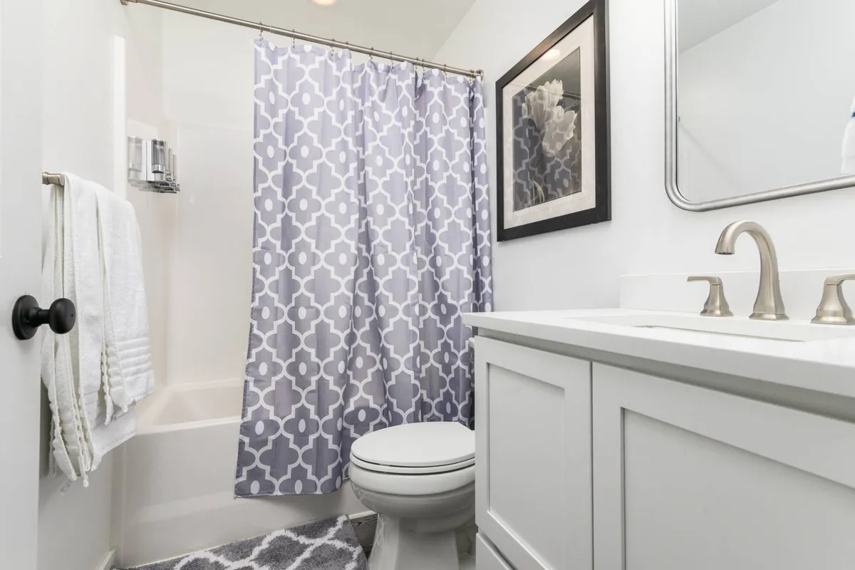 A calming bathroom scene with a bathtub, vanity, shower curtain, and framed artwork. The space is designed for comfort and relaxation, offering both functionality and a touch of luxury with its clean lines and thoughtful details.