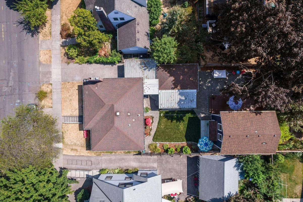 A wide exterior shot featuring the rooftops of neighboring houses, green spaces, and garden areas, creating a friendly, communal neighborhood feel. The image hints at backyard gatherings, barbecues, and connections to the outdoors.
