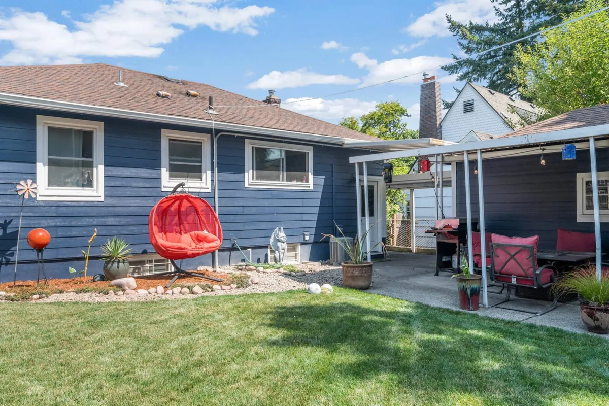 This cheerful exterior shot features a red hanging chair set on a green grass lawn adjacent to a patio seating area. Decorative stones and lush plantings add to the tranquil, inviting vibe, and the space is perfect for relaxing solo or gathering with friends.