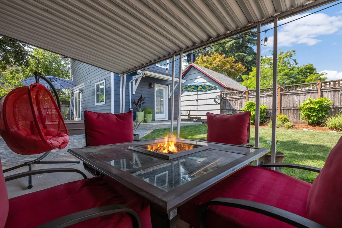 The image highlights a cozy outdoor space with a fire pit surrounded by red chairs, offering an inviting setting for evening gatherings, relaxing, and outdoor dining. The scene suggests warmth and intimate social moments under the stars.