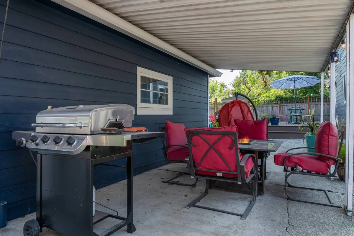 This image captures a vibrant outdoor dining area featuring a grill, red chairs, a dining table, and an umbrella set on a spacious deck. The scene exudes a casual yet inviting atmosphere perfect for barbecues, alfresco dining, and socializing with friends.